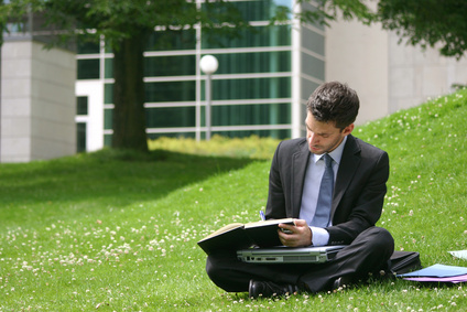 Mann sitzt mit Notebook auf einer grünen Wiese